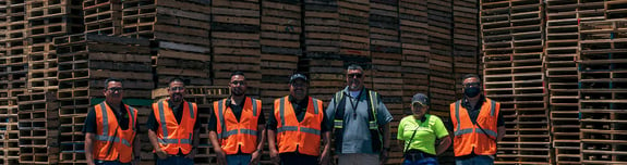 Six employees standing in front of pallets stacked high
